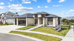 View of front of property with stone siding, a garage, a front yard, driveway, and roof with shingles