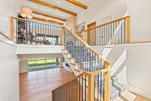 Stairs with beamed ceiling, wood finished floors, a chandelier, a high ceiling, and recessed lighting