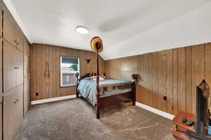 Carpeted bedroom with wooden walls and vaulted ceiling