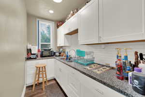 Kitchen with white cabinetry, decorative backsplash, light wood-style floors, light stone counters, and recessed lighting