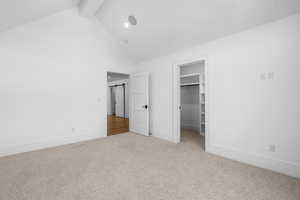 Unfurnished bedroom featuring beamed ceiling, carpet, high vaulted ceiling, a walk in closet, and a barn door