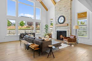 Living room featuring beamed ceiling, a stone fireplace, wood-type flooring, and high vaulted ceiling