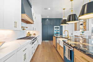 Kitchen featuring tasteful backsplash, light wood-style flooring, stainless steel appliances, custom range hood, and stone counters