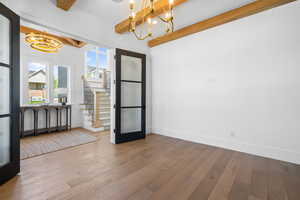 Unfurnished dining area featuring a chandelier, beamed ceiling, hardwood / wood-style flooring, and stairway