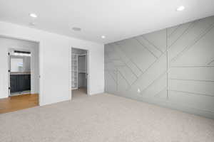 Unfurnished bedroom with carpet flooring, a spacious closet, recessed lighting, and a decorative wall