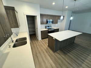 Kitchen featuring dark brown cabinets, appliances with stainless steel finishes, wood finished floors, light countertops, and recessed lighting