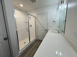 Full bath with a shower stall, wood finished floors, vanity, and recessed lighting