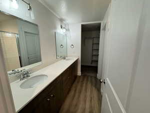 Full bath featuring a textured ceiling, a stall shower, double vanity, wood finished floors, and a walk in closet