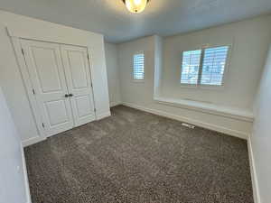 Unfurnished bedroom featuring dark carpet, a textured ceiling, and a closet
