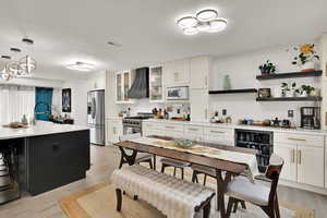 Kitchen with beverage cooler, custom exhaust hood, light wood finished floors, stainless steel appliances, and white cabinets
