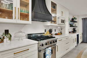 Kitchen featuring stainless steel range, custom exhaust hood, open shelves, white cabinets, and light wood-type flooring