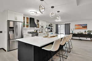 Kitchen featuring appliances with stainless steel finishes, light wood finished floors, custom exhaust hood, white cabinetry, and a textured ceiling