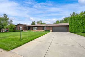 Single story home with an attached garage, driveway, a chimney, and a front lawn