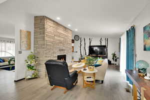 Living area with wood finished floors, a stone fireplace, and recessed lighting