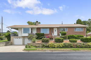 Ranch-style house with concrete driveway, a chimney, a garage, and brick siding