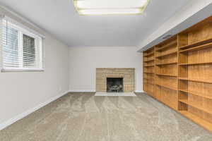 Unfurnished living room with carpet, a stone fireplace, and a textured ceiling