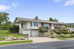 Ranch-style house featuring an attached garage, a chimney, concrete driveway, brick siding, and roof with shingles