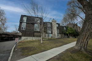 View of front of house with a front lawn, covered parking, a shingled roof, and a chimney