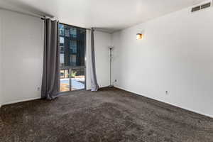 Spare room featuring dark colored carpet and expansive windows
