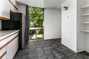 Kitchen with white cabinetry, freestanding refrigerator, light countertops, floor to ceiling windows, and open shelves