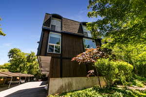 View of side of home with mansard roof, a shingled roof, and covered parking