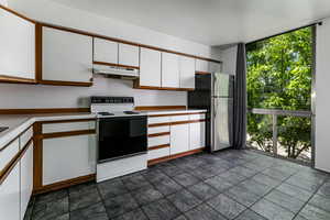 Kitchen featuring electric stove, white cabinetry, a wall of windows, under cabinet range hood, and light countertops