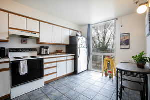 Kitchen with white electric range oven, under cabinet range hood, light countertops, white cabinets, and freestanding refrigerator