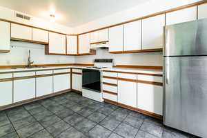 Kitchen with freestanding refrigerator, electric stove, light countertops, under cabinet range hood, and white cabinets