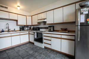 Kitchen featuring freestanding refrigerator, electric range, light countertops, under cabinet range hood, and white cabinets