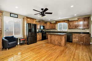 Kitchen featuring black appliances, dark countertops, hardwood floors, wooden cabinets, ceiling fan, and recessed lighting