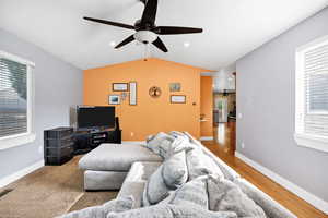 Living room, carpeted with lofted ceiling, a ceiling fan, and hardwood floors