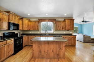 Kitchen with black appliances, plenty of natural light, open floor plan, brown wooden cabinets, hardwood floors, and a textured ceiling