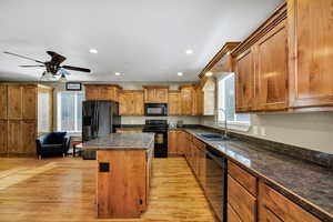 Kitchen with light hardwood flooring, a center island, black appliances, brown wooden cabinets, and recessed lighting