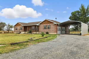 Ranch-style home with gravel driveway, a detached carport, covered porch, a front lawn, and brick siding
