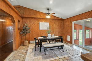 Dining room with lofted ceiling, wood walls, and ceiling fan