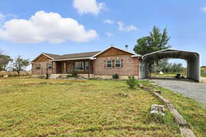 Ranch-style house featuring a carport, brick siding, gravel driveway, a porch, and a front lawn