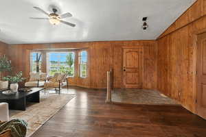 Living room featuring hardwood / wood-style floors, wooden walls, a ceiling fan, and lofted ceiling