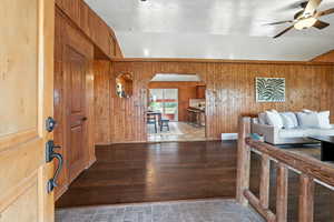 Foyer entrance featuring arched walkways, ceiling fan, wooden walls, lofted ceiling, and wood-type flooring