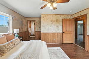 Bedroom with a wainscoted wall, dark wood finished floors, ornamental molding, wood walls, and a ceiling fan