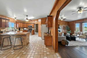 Kitchen featuring open floor plan, a ceiling fan, a peninsula, appliances with stainless steel finishes, and brown cabinets