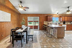 Dining space featuring ceiling fan, wooden walls, and vaulted ceiling