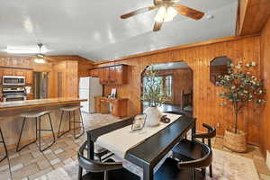 Dining area with ceiling fan, wooden walls, and lofted ceiling