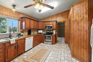 Kitchen featuring wood walls, stainless steel appliances, vaulted ceiling, brown cabinets, and decorative backsplash