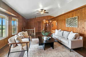 Living room featuring wooden walls, lofted ceiling, wood finished floors, and ceiling fan