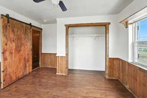 Unfurnished bedroom with wood walls, a wainscoted wall, wood finished floors, crown molding, and a closet