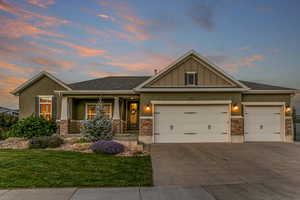 Craftsman-style home featuring an attached garage, driveway, stone siding, board and batten siding, and a front lawn