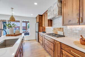 Kitchen with light wood finished floors, light countertops, custom range hood, brown cabinets, and tasteful backsplash