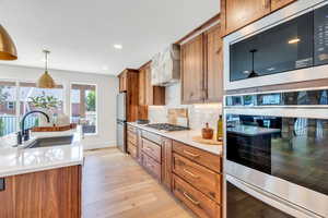 Kitchen featuring appliances with stainless steel finishes, brown cabinetry, light wood finished floors, light countertops, and backsplash