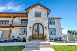 View of front of property with board and batten siding, a balcony, stone siding, and french doors