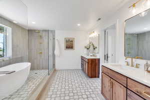 Bathroom featuring tiled shower, a freestanding bath, two vanities, recessed lighting, and tile walls